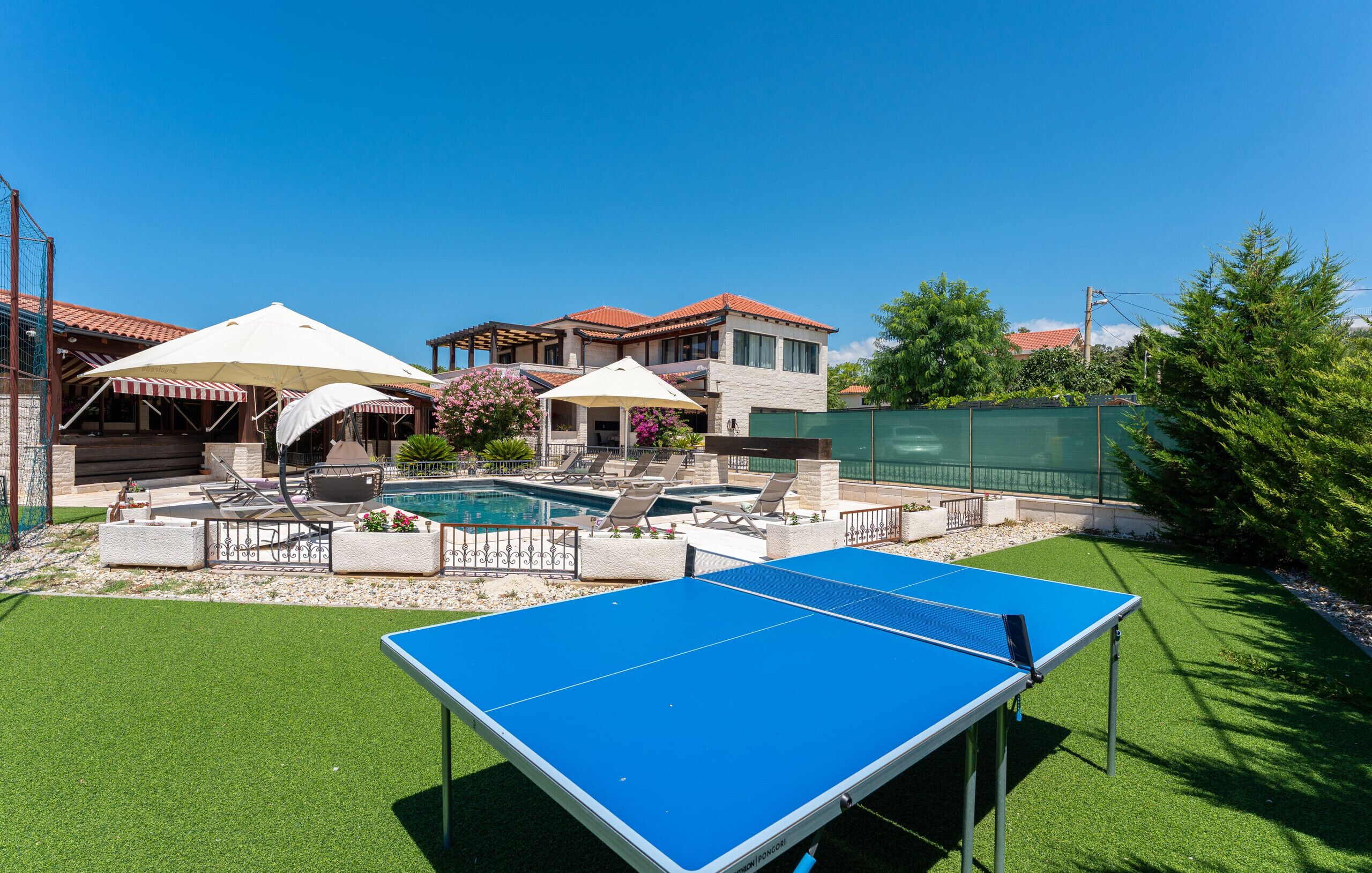 A pool area with a ping pong table, lounge chairs, and umbrellas.