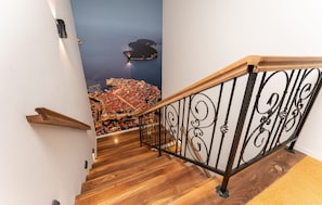 A wooden staircase with a black wrought iron railing, a wall mural of a coastal city, and a wooden handrail. - Villa Frenky (Vir)