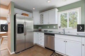A modern kitchen with white cabinets, stainless steel appliances, and a window providing natural light.