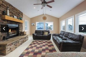 A living room with a fireplace, leather sofas, a patterned rug, and large windows.