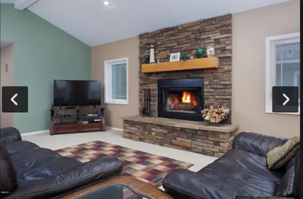 A living room with a stone fireplace, leather sofas, a flat-screen TV, and a patterned rug.