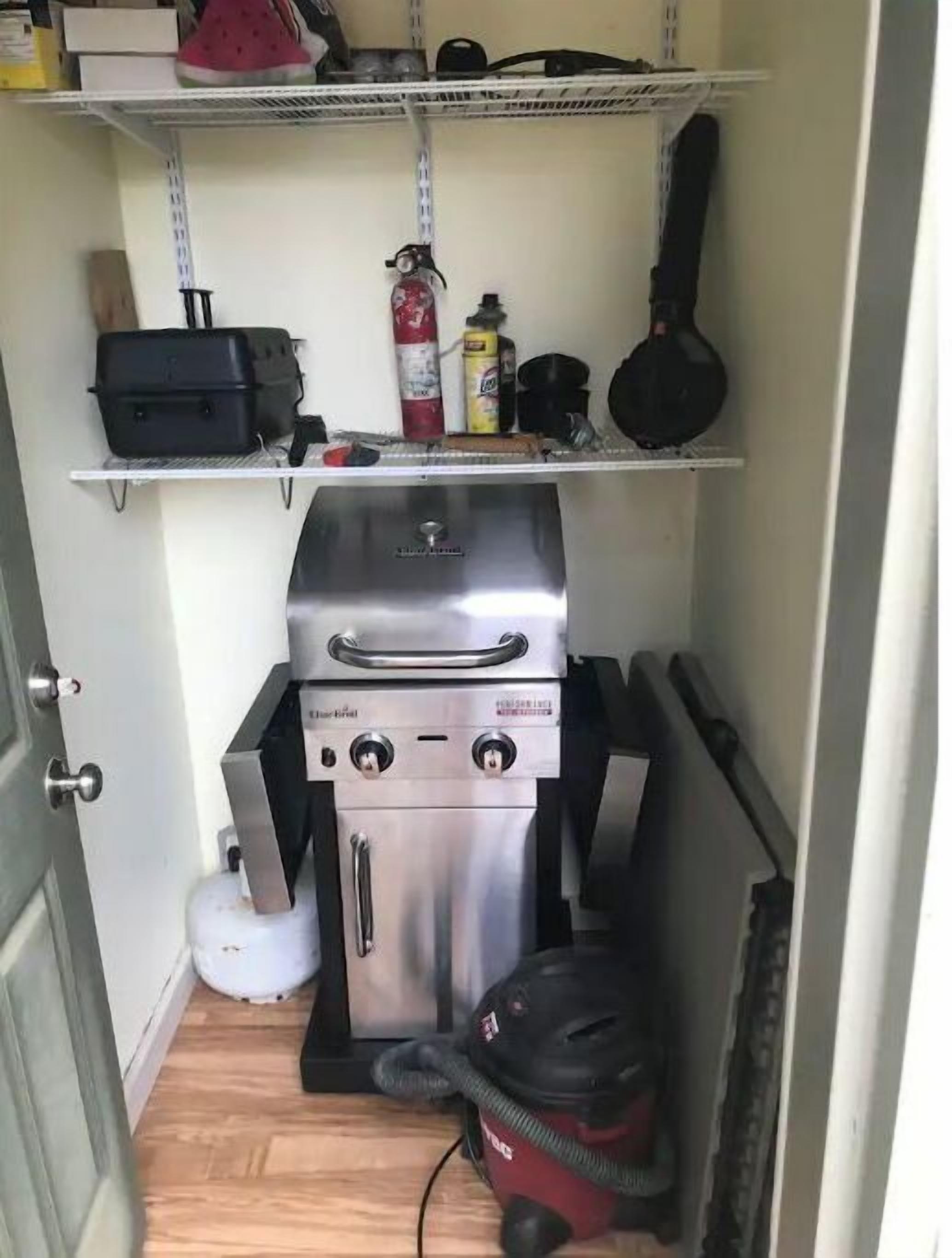 A compact kitchen with a built-in stainless steel grill, a white gas tank, and a black vacuum cleaner.