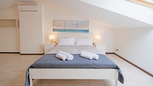 A modern bedroom with a bed, two bedside tables with lamps, a painting on the wall, and an air conditioning unit. - Casa Ruby - Pool and tennis court Lazise/Pacengo (Lazise)