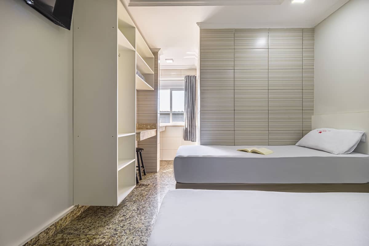 A modern hotel room with a large bed, a built-in wardrobe, and a small window.