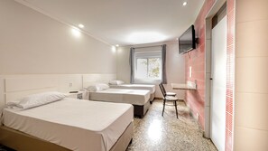 A hotel room with two beds, a desk, a chair, a TV mounted on the wall, and a window with curtains. - Hotel Monte Palma (São Paulo)