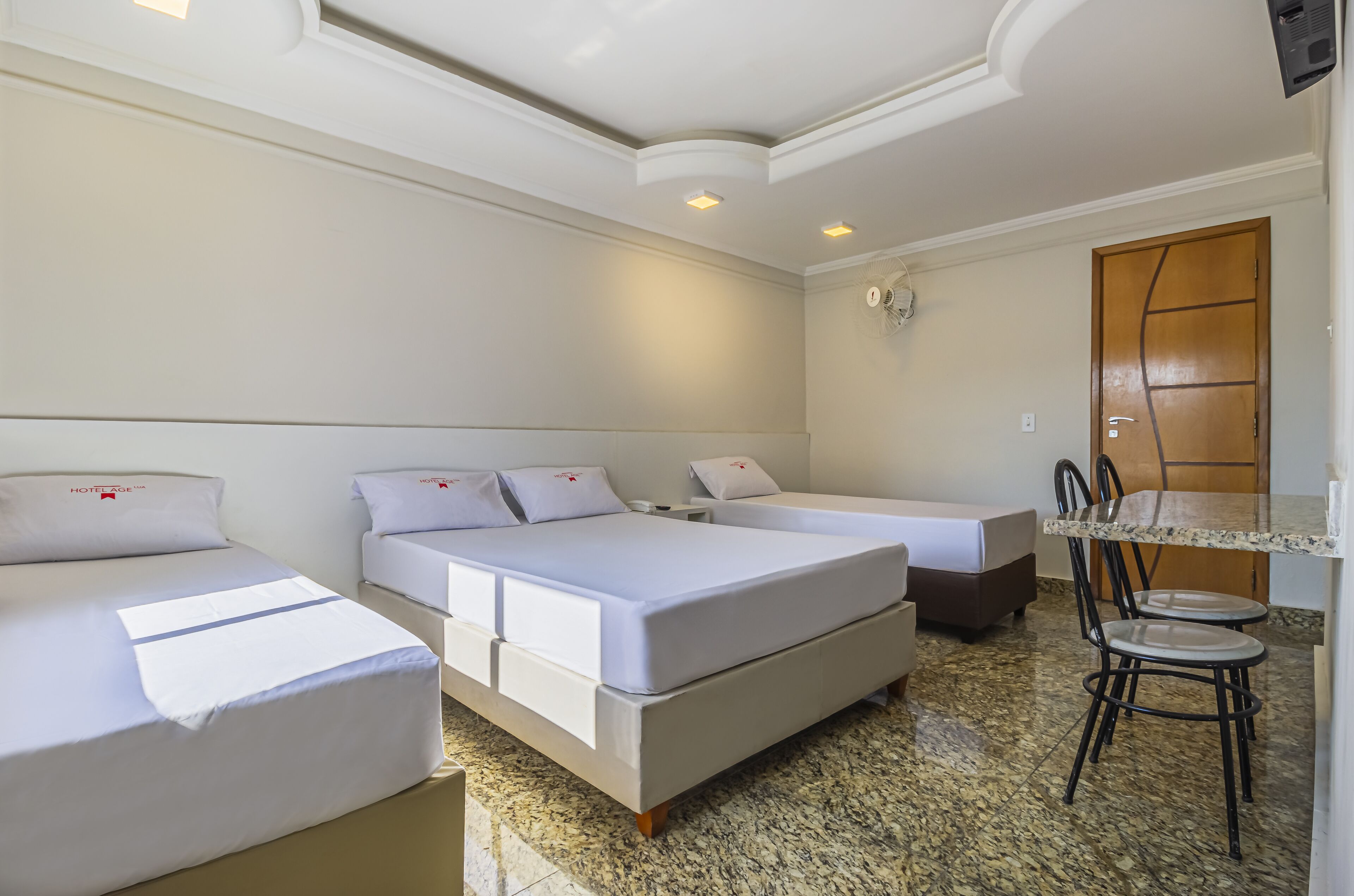 A hotel room with two single beds, a small desk with a chair, and a wooden door.