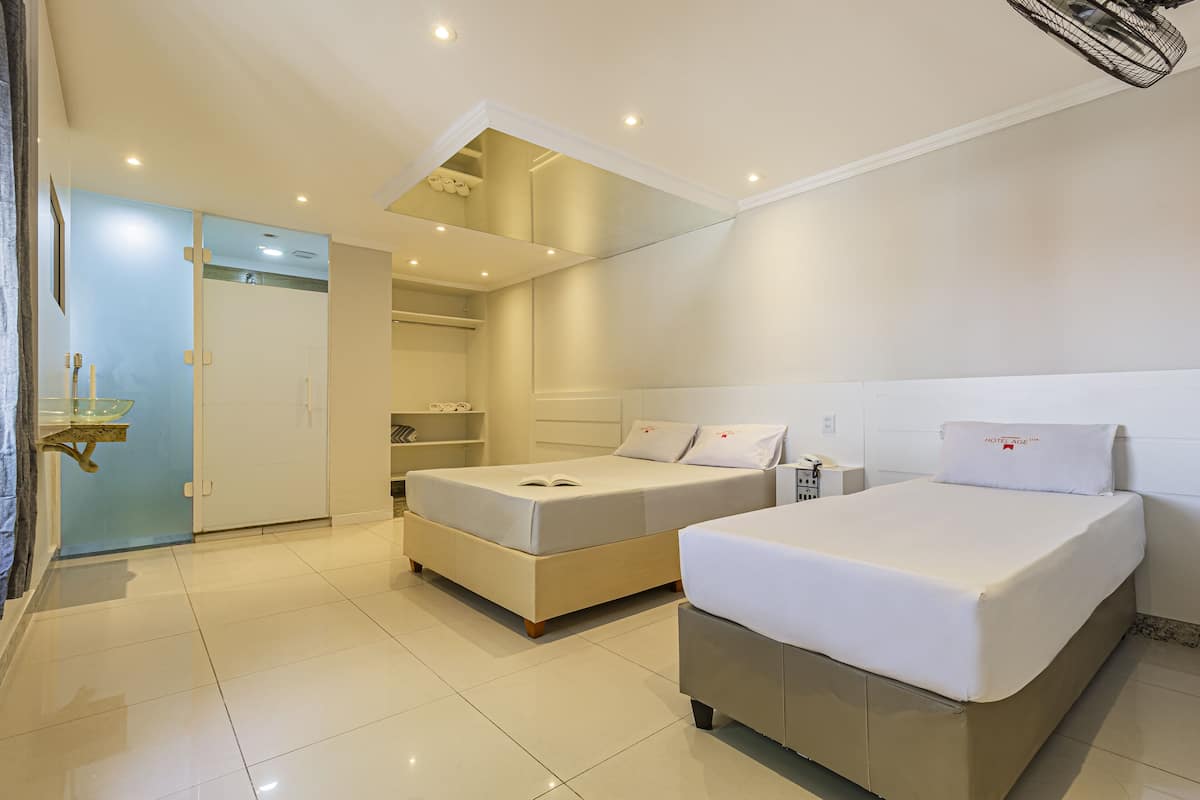 A modern hotel room with a large bed, a smaller bed, a wardrobe, and a mirror.