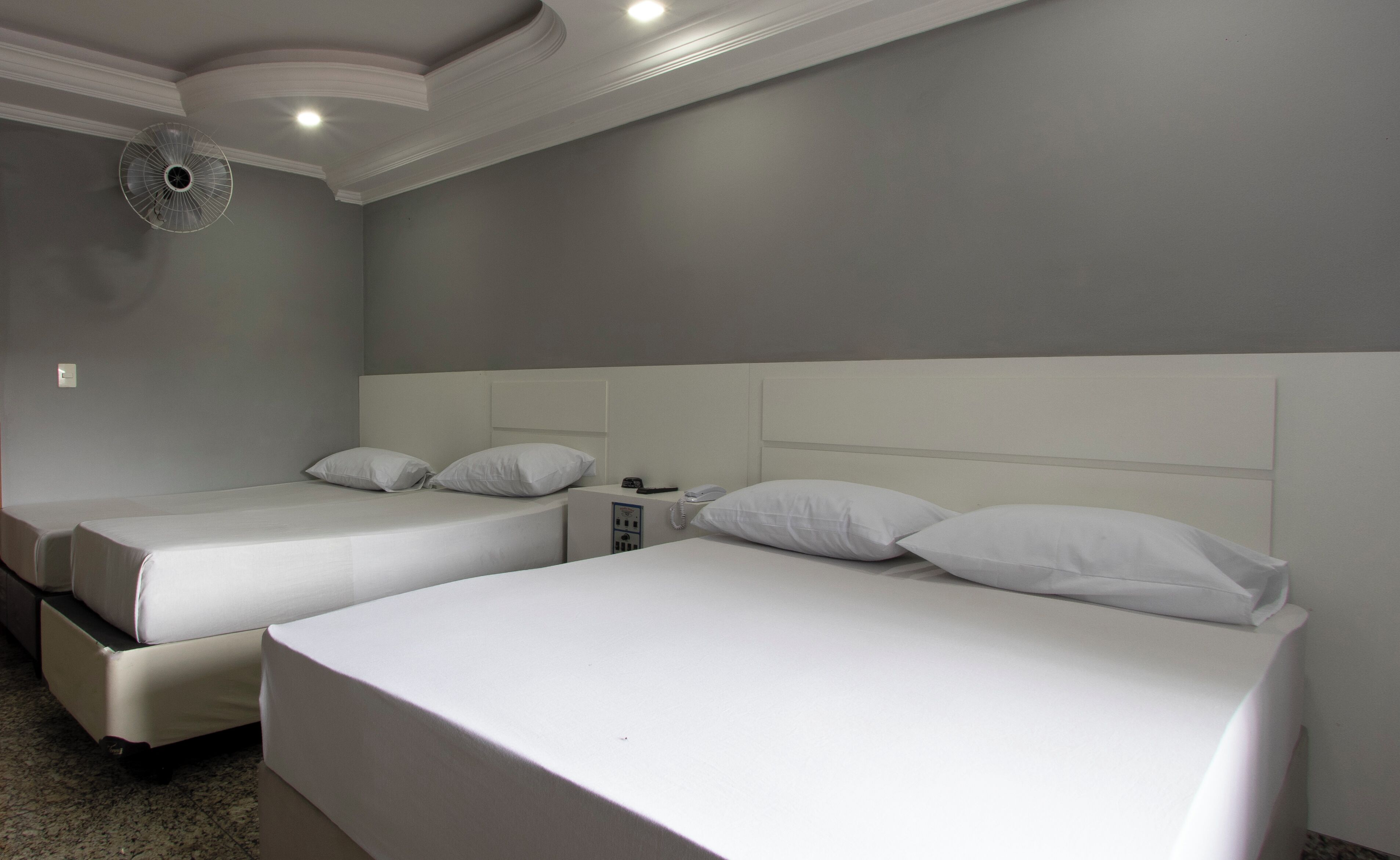 Hotelkamer met twee enkele bedden, elk voorzien van witte lakens en kussens, een klein nachtkastje met een telefoon en een plafondventilator.