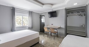 A hotel room with a bed, a desk, two chairs, a TV, and a wardrobe. - Hotel Monte Palma (São Paulo)