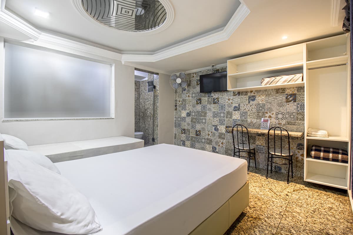 A bedroom with a bed, a TV, a desk with chairs, and a wardrobe.