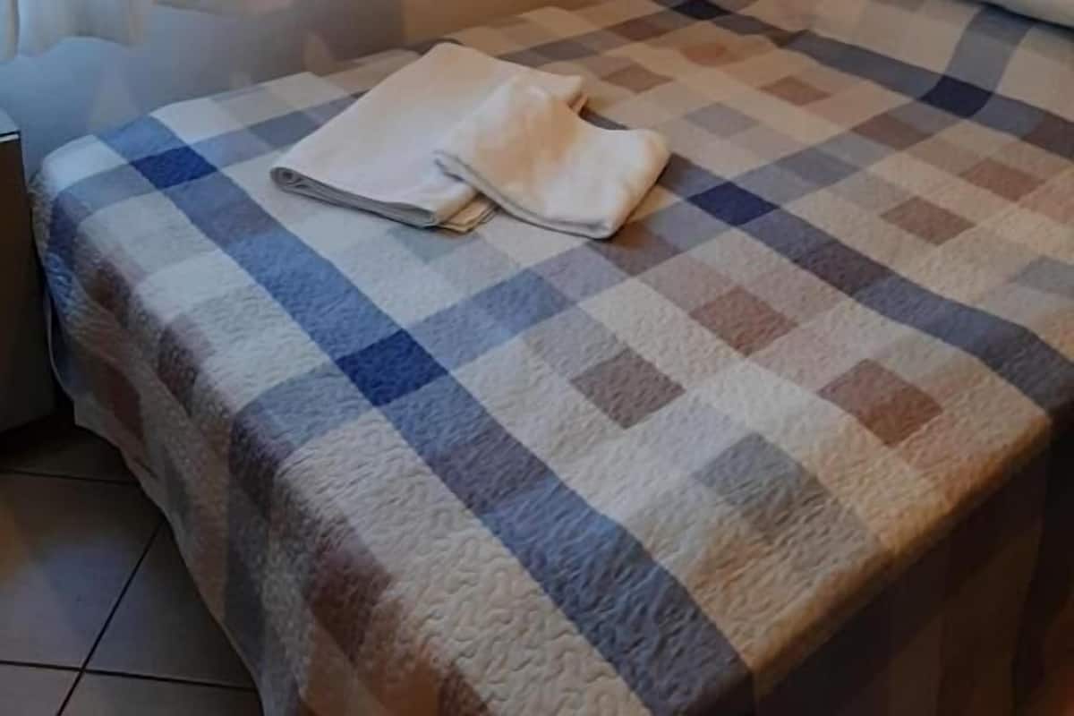 A neatly made bed with a checkered bedspread, a pillow, and a folded blanket on the bed.