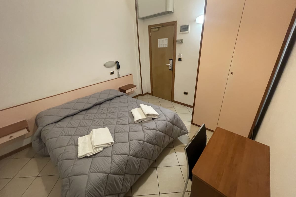 A bedroom with a bed, a bedside table, a wooden nightstand, a wardrobe, and a door with a lock.