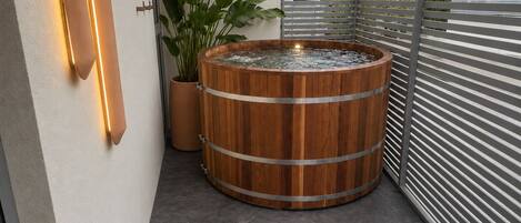 Un espacio de spa con un jacuzzi de madera, una planta en maceta y una lámpara moderna.