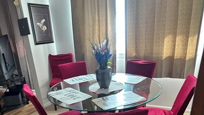 Un tavolo rotondo in vetro con un vaso di fiori, circondato da sedie rosse in una stanza con tappeto beige.