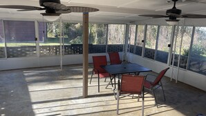 Un patio coperto con tavolo e sedie, ventilatori a soffitto e ampie finestre che si affacciano sull'esterno.