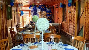 A dining area with round tables set for a meal, wooden chairs, and a decorative wall with hanging balloons. - Pensiunea GuestHouse (Stănești)