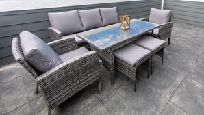 An outdoor patio with wicker furniture, a glass-top table, and grey cushions. - Luxury 3BR/4BA Townhome • Rooftop Deck, Porch • 5 Min to Downtown (Omaha)