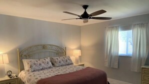 A bedroom with a bed, nightstands, a ceiling fan, and a window with curtains. - Minutes from the beach! Private pool and game room (Cape Coral)
