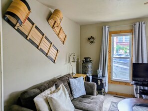 A living room with a sofa, a television, a window with curtains, and wall-mounted wooden decorations.