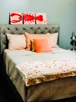 A bedroom with a tufted headboard, a bed with a white and orange floral bedspread, and three red artwork pieces on the wall. - In the heart of Cajun country! Entire home with pool. (Breaux Bridge)