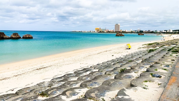 A beach with clear turquoise water, a sandy shore, and a stone pathway leading to the water. - HOTEL ARENA (Chatan)
