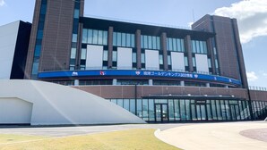 A modern building with a glass facade, large windows, and a blue sign with white text. - HOTEL ARENA (Chatan)