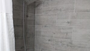 Un baño con baldosas de madera grises, una ducha con cabezal de ducha de mano, un inodoro y un piso con estampado de cuadros.