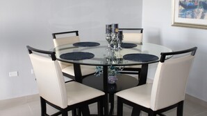 Una mesa redonda de cristal con cuatro sillas, un jarrón con flores y un cuadro en la pared.