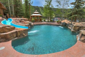 A clear blue pool with a waterfall feature, surrounded by rocks and a gazebo.