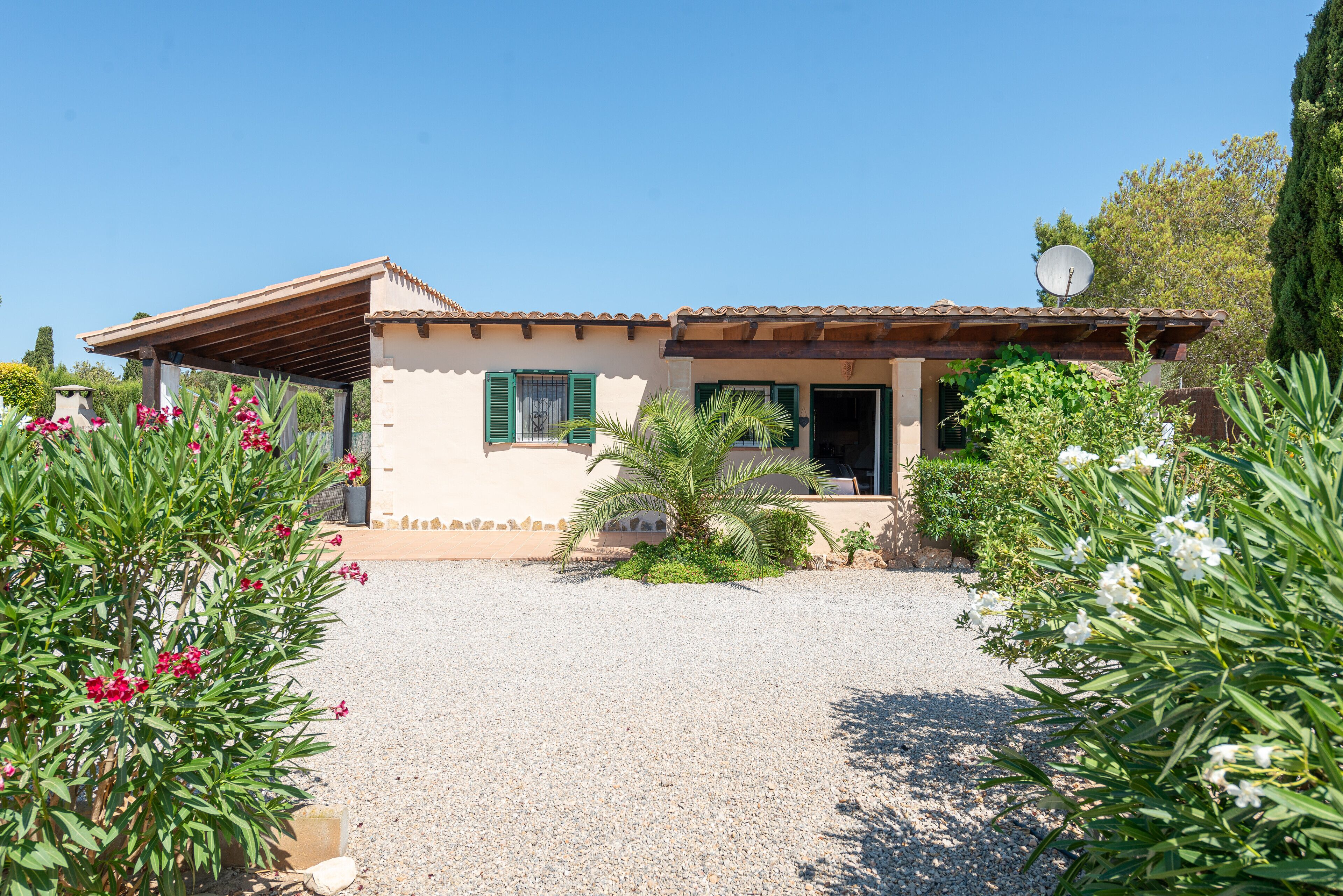 A house with a gravel driveway, a satellite dish, and a palm tree in the front yard.