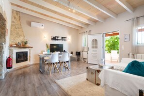 A living room with a stone fireplace, a dining area with chairs, a television, and a view of the outdoors.