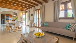 A spacious living area with a sofa, dining table, and chairs. There is a kitchen visible in the background.
