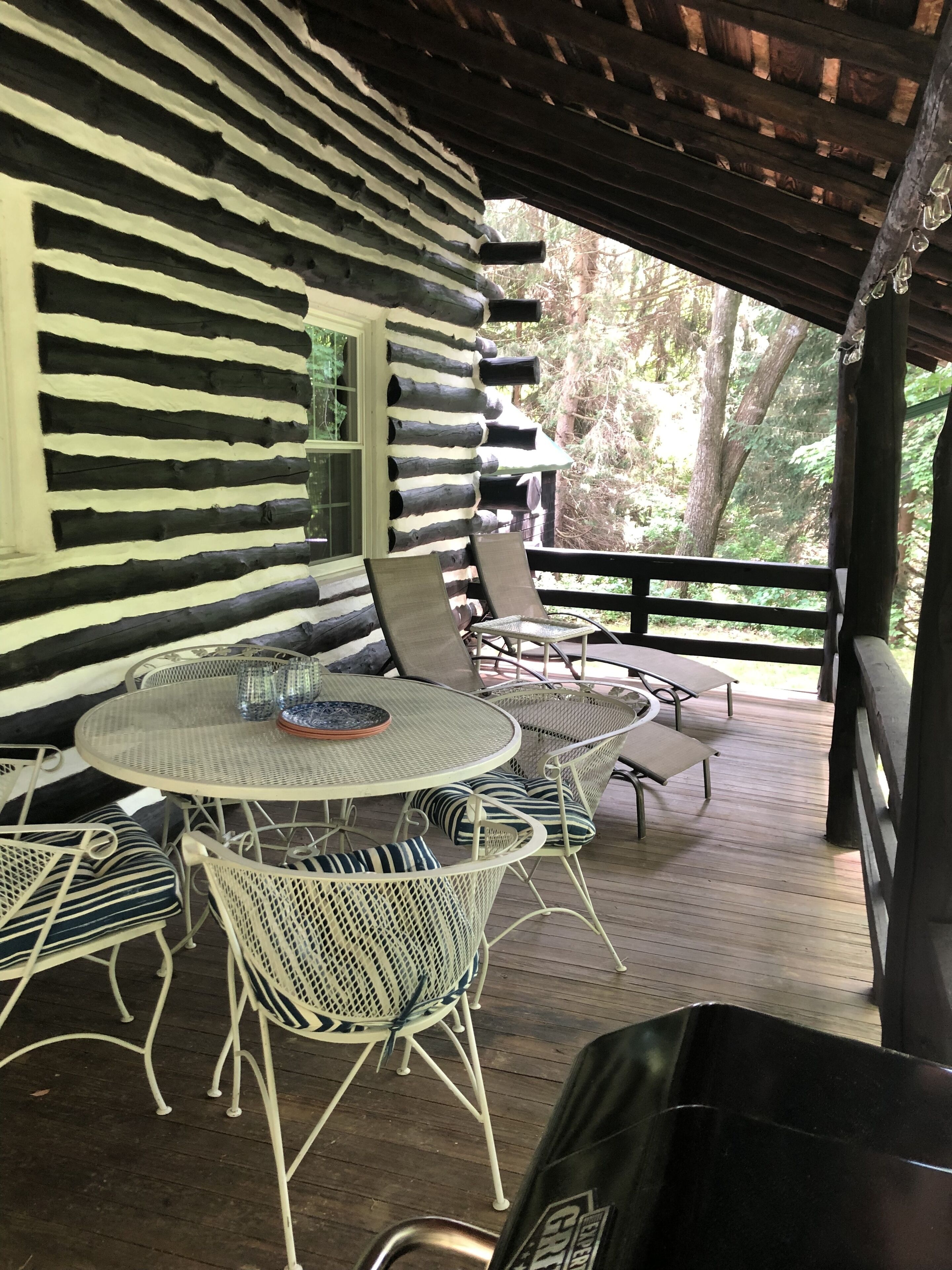 A log cabin with a covered porch, outdoor seating, and a grill.