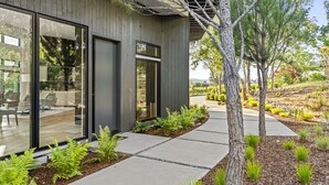 A modern building with large glass windows, a concrete pathway, and a variety of greenery including ferns and small trees. - The Quails Crossing-Healdsburg Vineyard Home (Healdsburg)