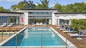 A modern outdoor pool area with lounge chairs and umbrellas, surrounded by a wooden deck and a building with large windows. - The Quails Crossing-Healdsburg Vineyard Home (Healdsburg)
