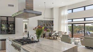 A modern kitchen with a large island, stainless steel appliances, and a dining area with a view of the outdoors. - The Quails Crossing-Healdsburg Vineyard Home (Healdsburg)