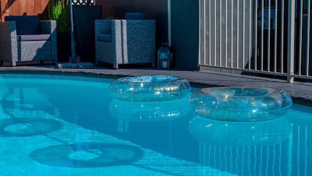 A swimming pool with two inflatable rings, lounge chairs, and a wooden deck.