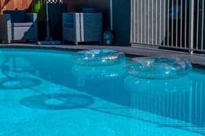 A swimming pool with two inflatable rings, lounge chairs, and a wooden deck.