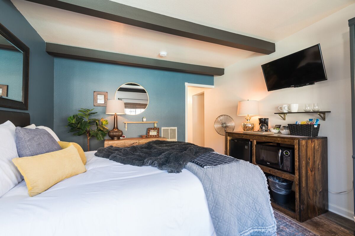A bedroom with a bed, bedside table, lamp, TV, and a wooden cabinet with a microwave.