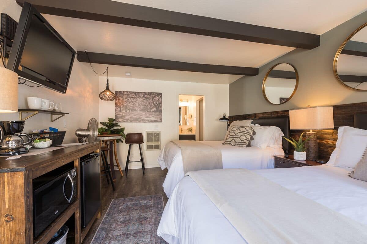 A hotel room with a bed, bedside tables, a TV, a desk with a computer, and a chair.