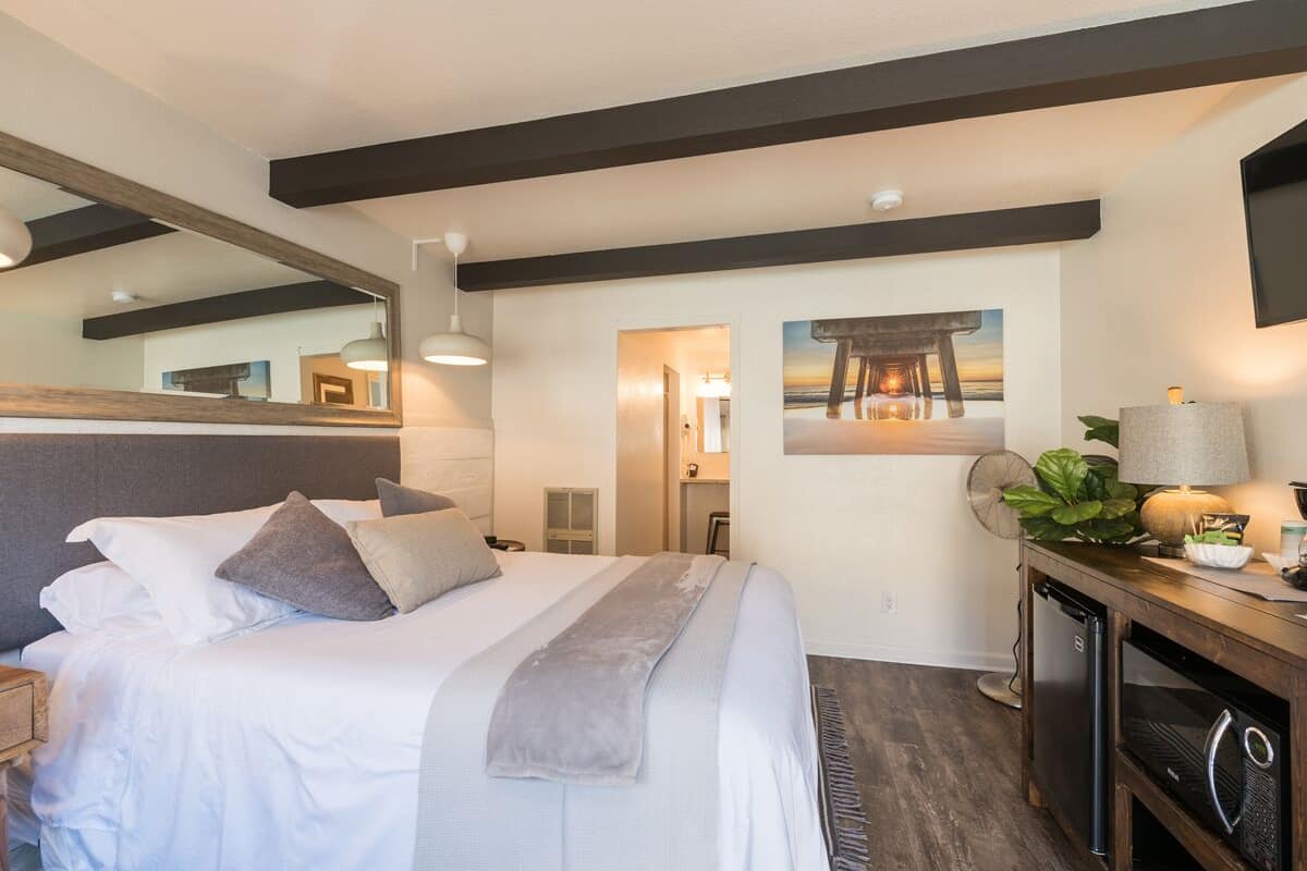 A bedroom with a bed, bedside table, lamp, and a large mirror.