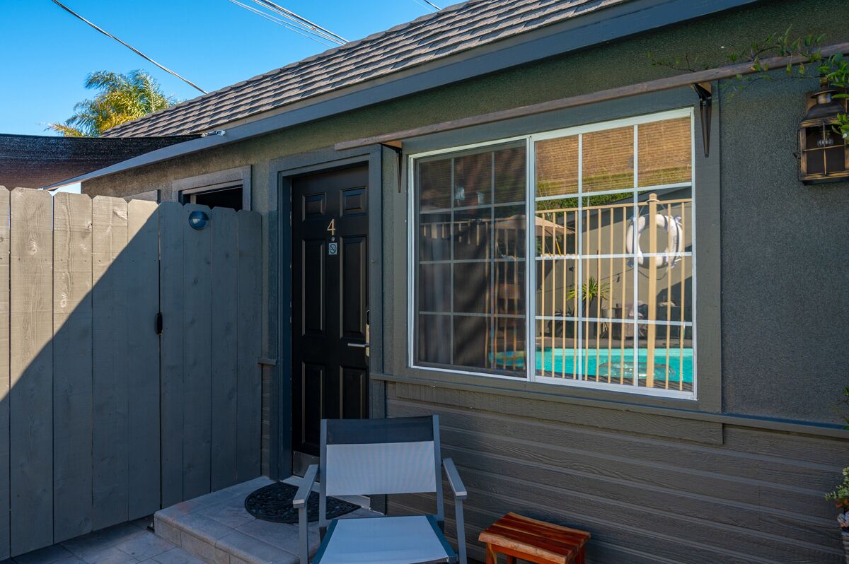 Uma casa pequena com uma porta escura, uma janela com grade de metal e um pequeno pátio com uma cadeira e mesa.