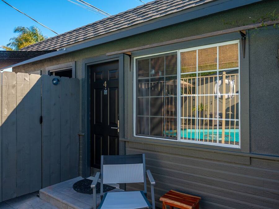 Uma casa pequena com uma porta escura, uma janela com grade de metal e um pequeno pátio com uma cadeira e mesa.