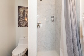 A bathroom with a toilet, a shower with a marble wall, and a towel rack.