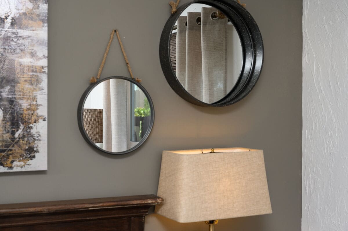 Two round mirrors on a wall, a lamp, and a piece of abstract art.