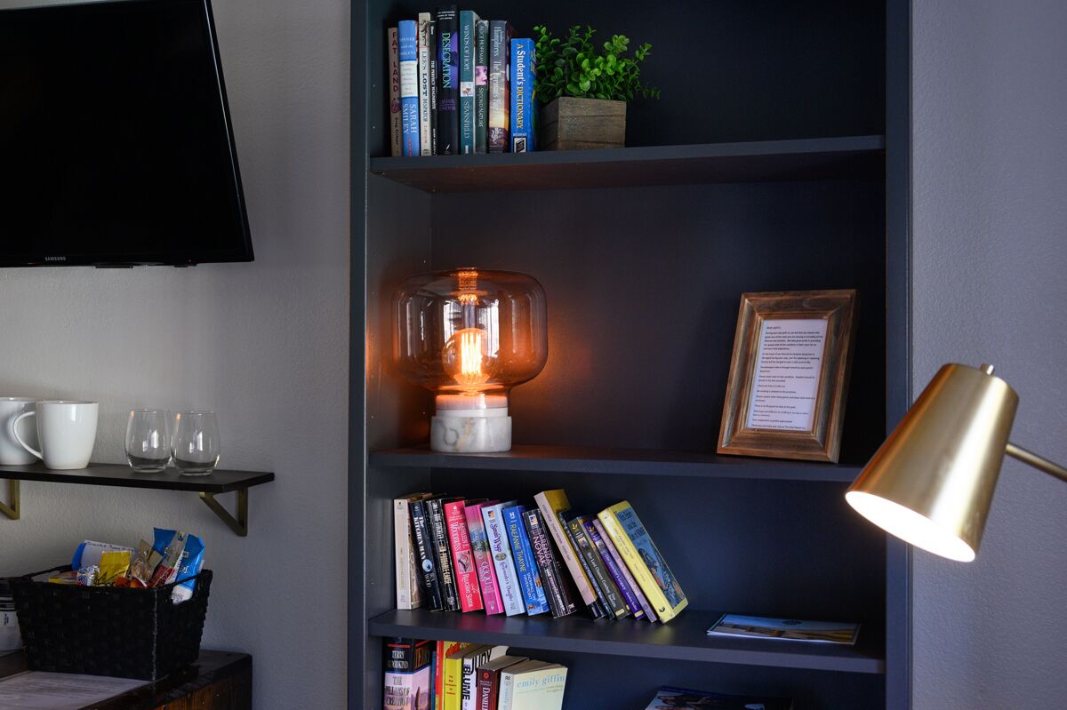 A bookshelf with books, a framed certificate, and a table lamp.