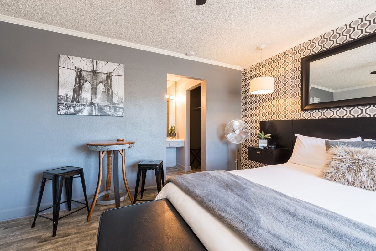 Hotelkamer met een bed, een bureau, twee krukken, een spiegel en een ventilator aan de muur.