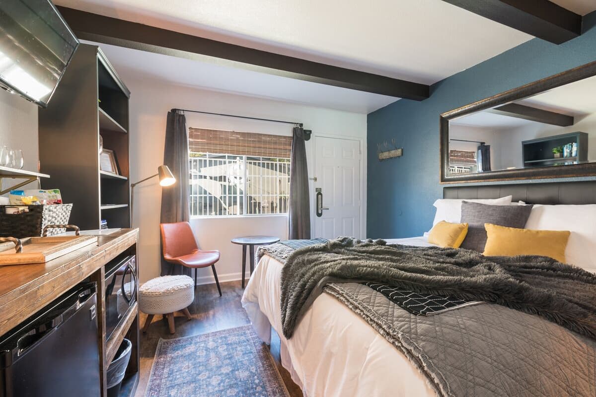 A bedroom with a bed, bedside table, chair, and a window with a view of a white car.