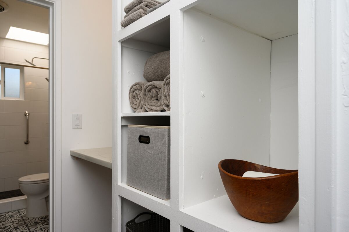 A bathroom with a toilet, a shower, and a shelf with towels and a storage box.