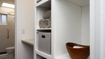 A bathroom with a toilet, a shower, and a shelf with towels and a storage box.